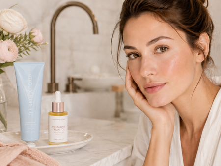 Woman sitting by bathroom bench with Hydrating Body Lotion and Hydrating Facial Oil on the bench.